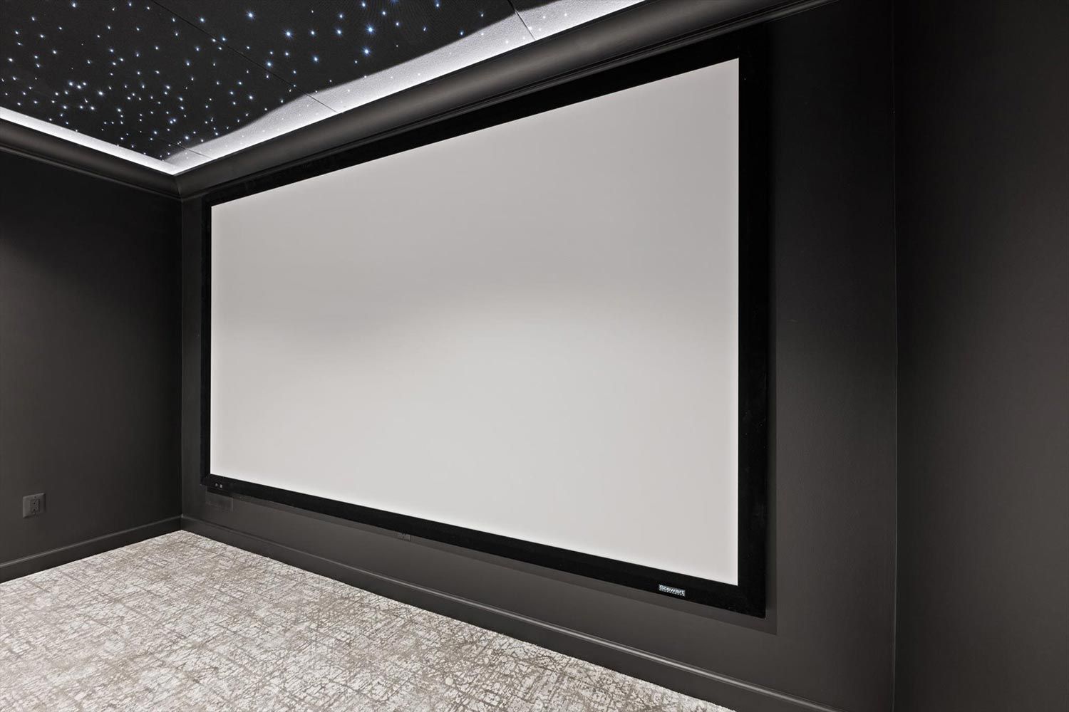 Spacious home theater room with a large projection screen, complemented by a ceiling that mimics a star-filled sky, creating an immersive viewing experience.
