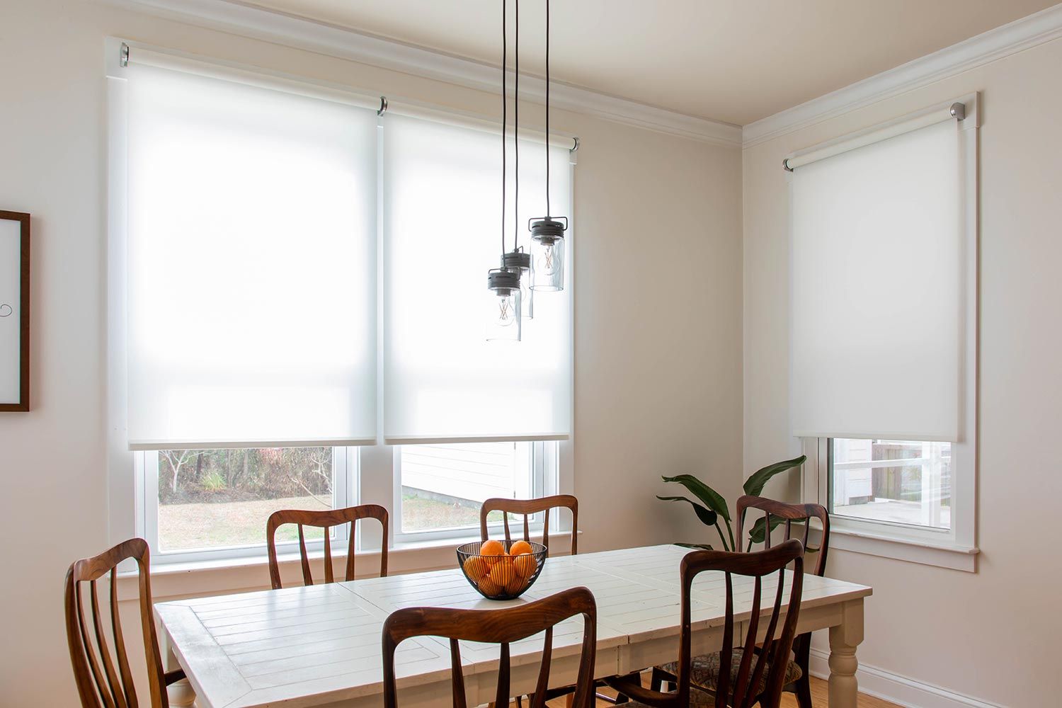 Dining area with Savant white motorized window shades, wooden chairs, and a white dining table.