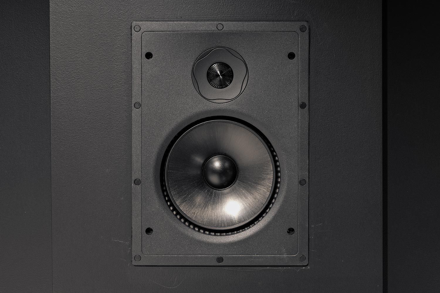 Detailed close-up of a wall-mounted speaker in a home theater, highlighting the precision and quality of the audio equipment installed.